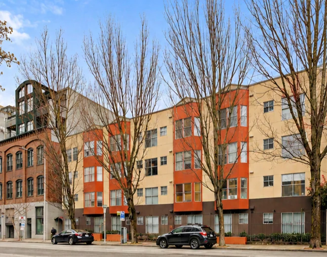 Nordic Bay at 2510 Western Ave: a four-story brick and stucco mid-rise with orange bays on a tree-lined Belltown street.